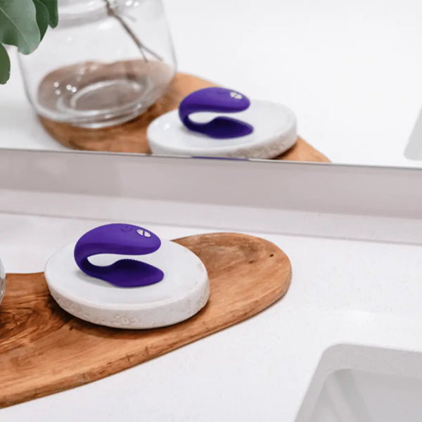Purple We-Vibe Sync resting on marble dish atop wooden tray in a bathroom setting