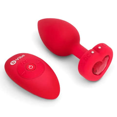 Red silicone vibrating plug with heart-shaped jewel base beside oval wireless remote control