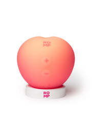 ROMP Pink Peach clitoral stimulator on white circular charging dock, front button view