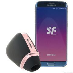 Satisfyer Love Triangle black air pulse stimulator beside a Samsung phone showing the SF Connect app