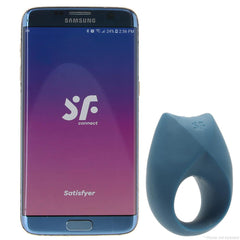 Satisfyer Royal One ring vibrator in slate blue beside a Samsung smartphone showing the SF Connect app