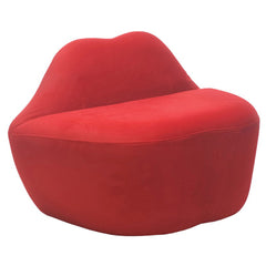 Side-angle view of red velvet lip-shaped loveseat showing smooth curved backrest and base