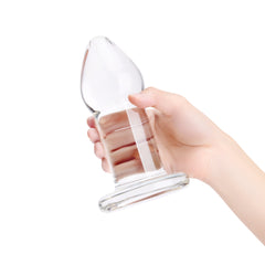 Side view of clear glass anal plug held in hand, showing full length and flat base