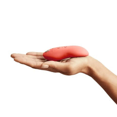 Side profile of coral Touch X vibrator resting in a hand, showing slim low-profile form factor