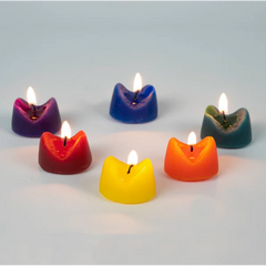 Six multicolored anus-shaped candles with lit flames displayed on a light surface