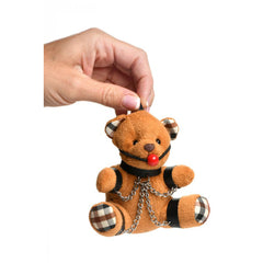 Small plush bear keychain held by hanging loop, displaying chain details and black faux-leather straps
