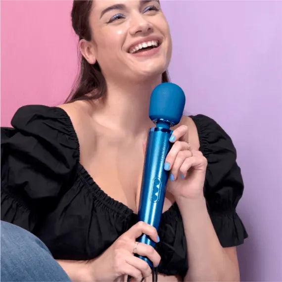 Smiling woman in black top holding Le Wand Pacific Blue massager against pink background