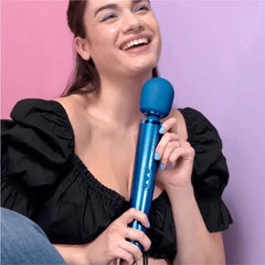 Smiling woman in black top holding Le Wand Pacific Blue massager against pink background