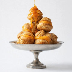 Stack of cream puffs with caramel drizzle on a silver pedestal stand evoking the lubricant's bakery scent