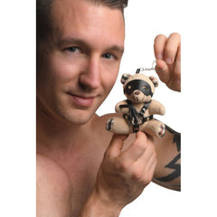 Tattooed man holding BDSM teddy bear keychain by silver key ring, showing small compact size
