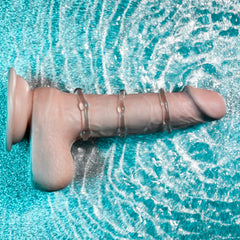Three clear beaded cock rings stacked on a realistic dildo against a water background