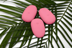 Three pink Je Joue ILY Pebble vibrators arranged on tropical palm leaves