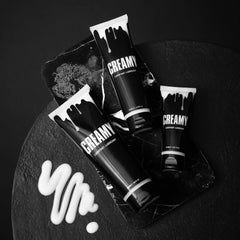 Two Creamy lubricant tubes arranged on dark stone surface beside white cream texture swatch