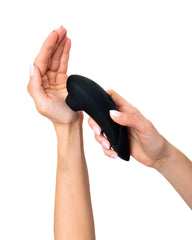 Two hands demonstrating the compact size and ergonomic grip of the black stimulator