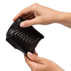 Two hands flexing the removable black silicone sleeve of the Zing stroker to show material flexibility