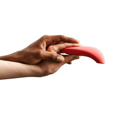 Two hands holding the curved coral silicone We-Vibe Melt, showing flexible soft texture