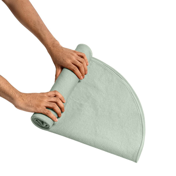 Two hands rolling the round sage green blanket for compact storage after use