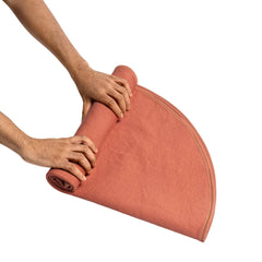 Two hands rolling the round waterproof blanket, demonstrating compact and easy storage