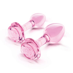 Two pink glass butt plugs with sculpted rose bases shown side by side out of packaging