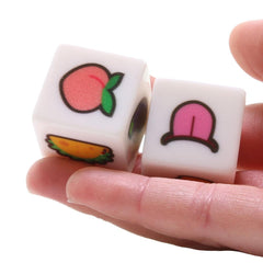 Two white emoji dice held in hand revealing peach and tongue emoji faces on each side
