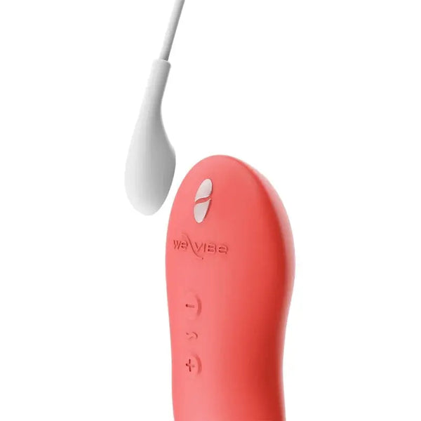 We-Vibe Touch X in coral connected to its magnetic USB charging cable at the charging port