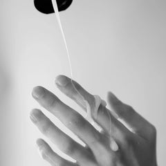 White creamy lubricant dispensing from black tube cap onto open hand, showing fluid consistency