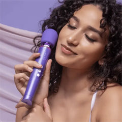 Woman with curly hair holding Le Wand Petite Massager near cheek, eyes closed, relaxed expression