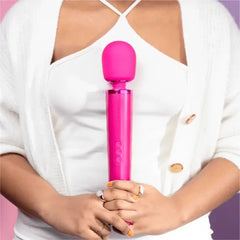 Woman in white outfit holding magenta Le Wand wand massager upright at chest level