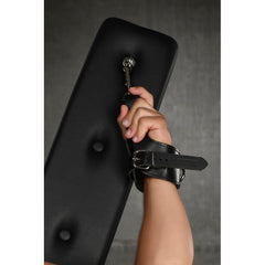 Wrist restrained with leather cuff clipped to D-ring anchor point on black padded arm pad